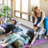 Woman in Supported Constructive Rest Pose/Savasana with Standard Bolster - Olive, Peachskin Eye Pillow - Amethyst, Pranayama Bolster - Night Flight, Sandbag - Gray