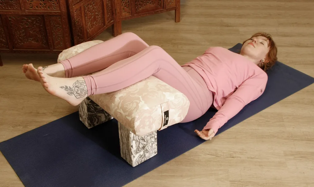 Savasana with Legs in Restorative Bench with Blush Bouquet Standard Bolster and Storm Marbled Foam Blocks
